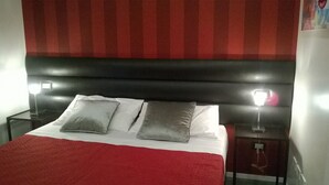 Un llit amb dos coixins, una manta vermella i un capçal de llit negre. Hi ha dues làmpades de nit a banda i banda del llit.