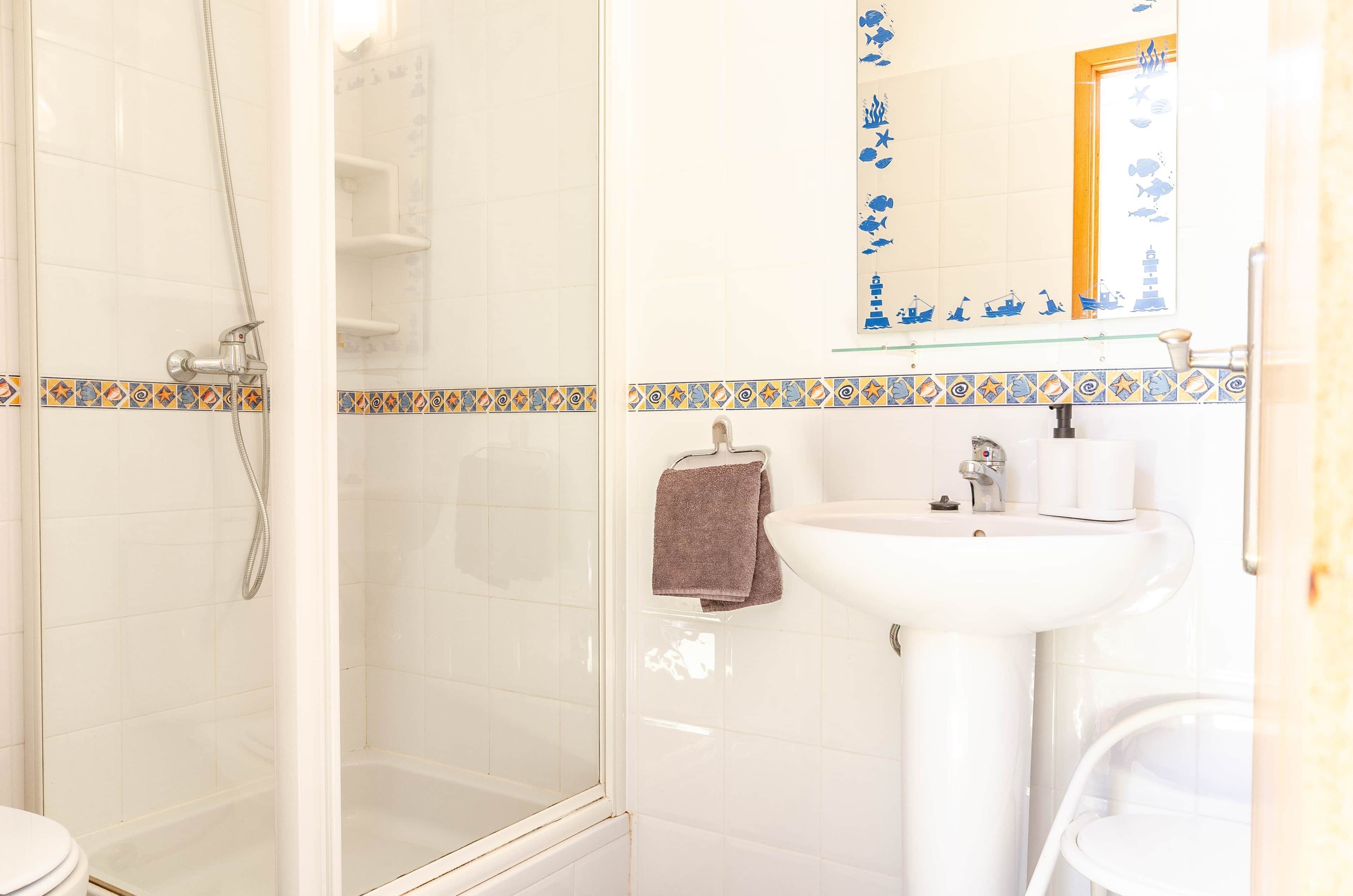 Een badkamer met een glazen douchecabine, een wit wastafelmeubel en een spiegel met een decoratieve tegelrand.