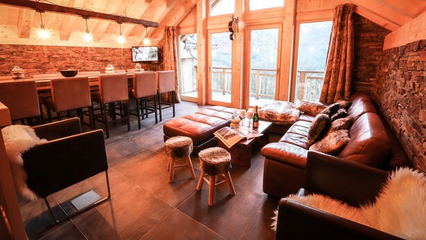 Ein gemütlicher Innenraum mit Holzbalkendecke, einer Bar, Ledersitzmöbeln und einer Steinwand.