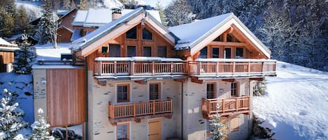 Un edificio de estilo chalé con balcón, rodeado de árboles cubiertos de nieve y un paisaje montañoso.