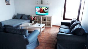 Una sala de estar con un sofá gris, una mesa de centro y un televisor sobre un mueble.