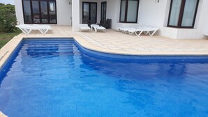 Una piscina rectangular con borde de azulejos, rodeada de baldosas color beige.