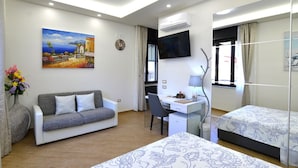 A hotel room with a sofa, a desk, a bed, a TV, and a painting on the wall.