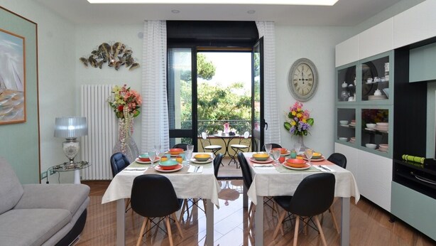 A dining area with a table set for four, a sofa, a radiator, a clock, and a view of the outdoors.