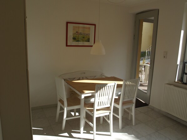 Un comedor con una mesa de madera y sillas blancas, un cuadro en la pared y una ventana con vistas al exterior.