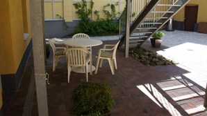 Un espacio al aire libre con patio, mesa, sillas, una escalera y plantas en macetas.