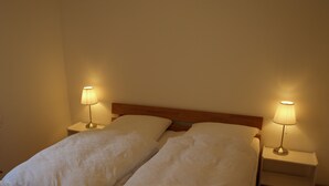 Cama doble con sábanas blancas y dos lámparas de noche sobre mesitas de madera.