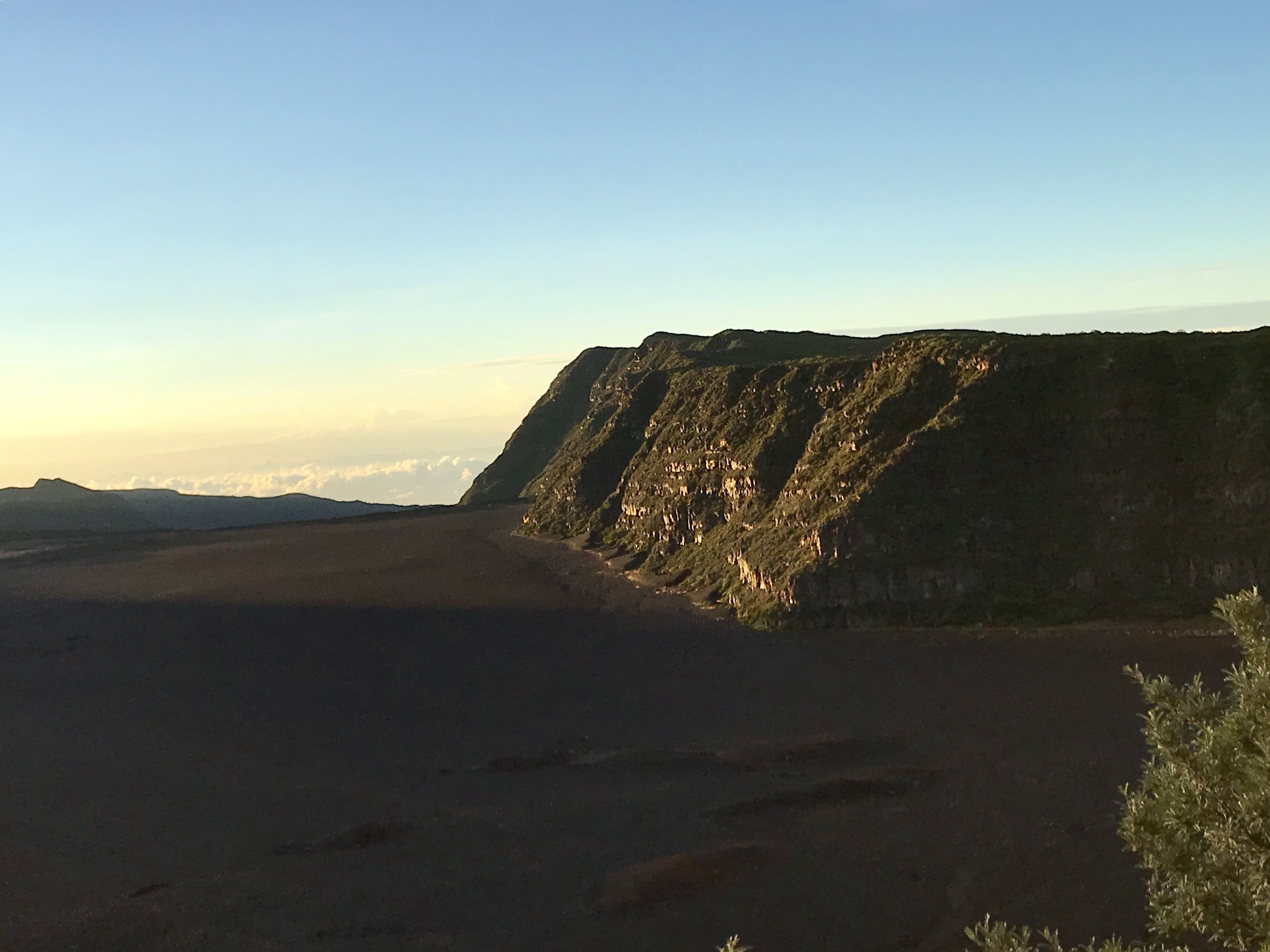 Un paysage désertique avec une falaise imposante et un ciel dégagé.