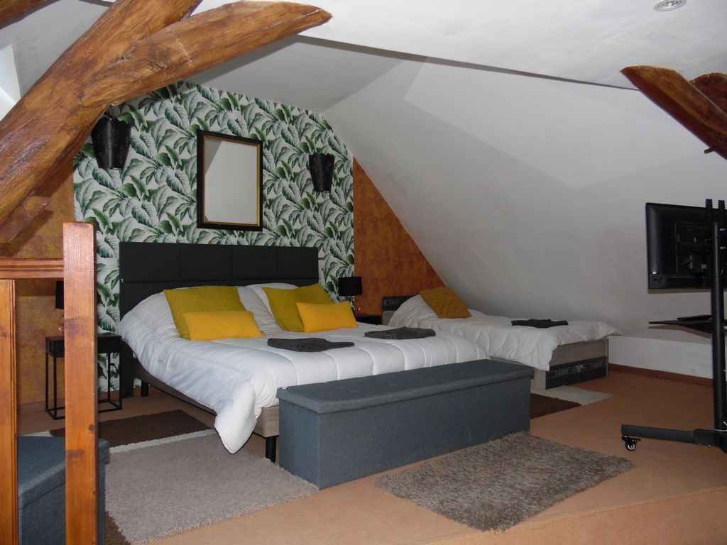 Ein Schlafzimmer mit schrägemausertem Dach, einem Bett mit weißer Bettwäsche und gelben Kissen, einer kleinen Bank und einem Fernseher auf einem Schrank.
