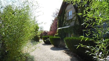 Ein Kiesweg führt zu einem Gebäude mit einer Steinaußenwand, umgeben von ordentlich geschnittenen Hecken und Bambuspflanzen.