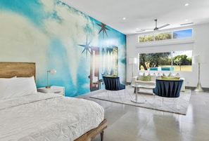 A modern hotel room with a large bed, a desk, a chair, and a view of the outdoors.