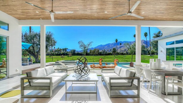 Un'area esterna moderna con piscina, mobili bianchi e vista sulle montagne e sul verde.