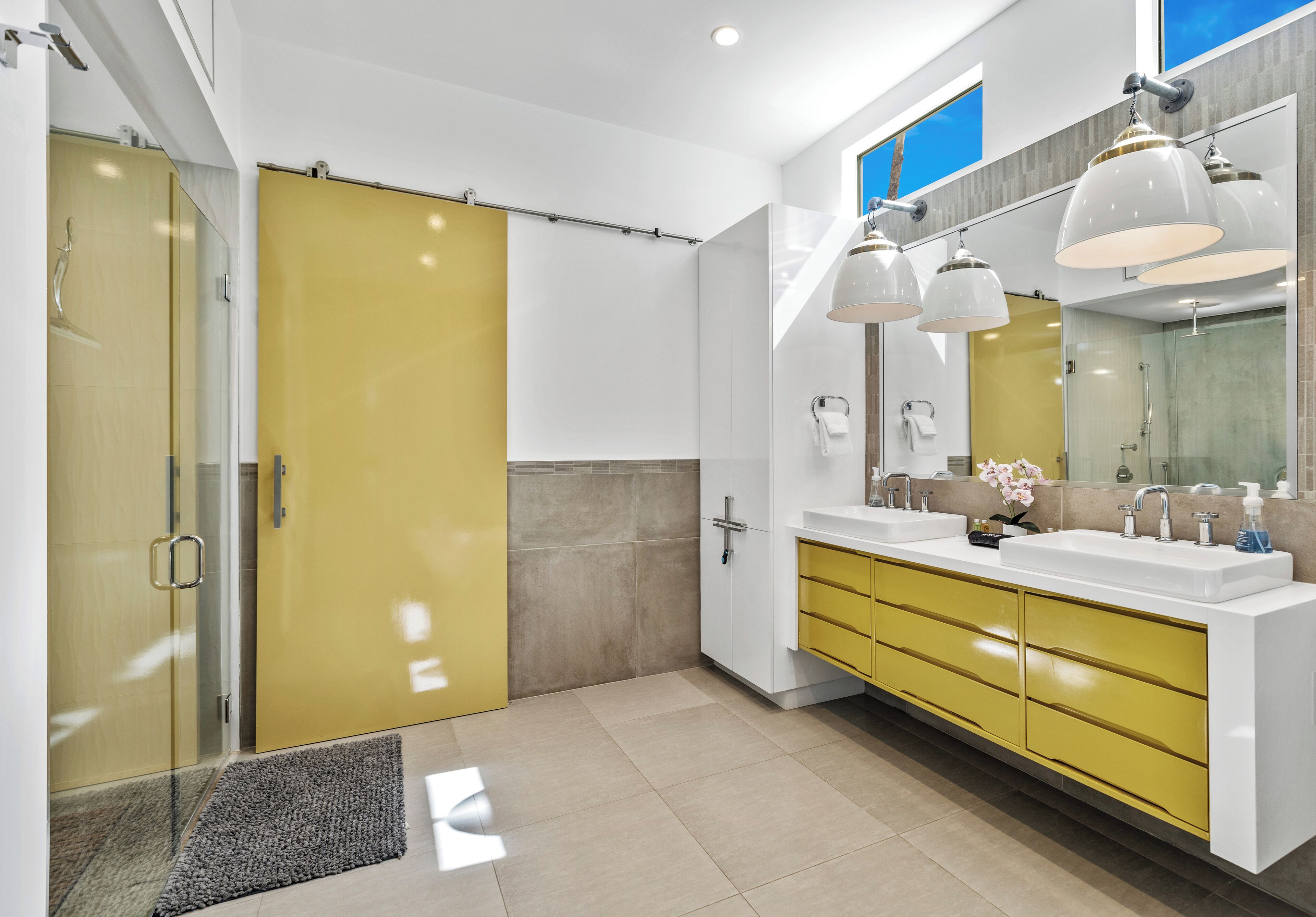 A modern bathroom with a yellow vanity, a large mirror, and a shower area.
