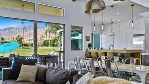 Un soggiorno moderno con un'ampia finestra che si affaccia su un campo da golf, una zona pranzo con cucina sullo sfondo e un angolo salotto accogliente con una coperta di pelliccia.