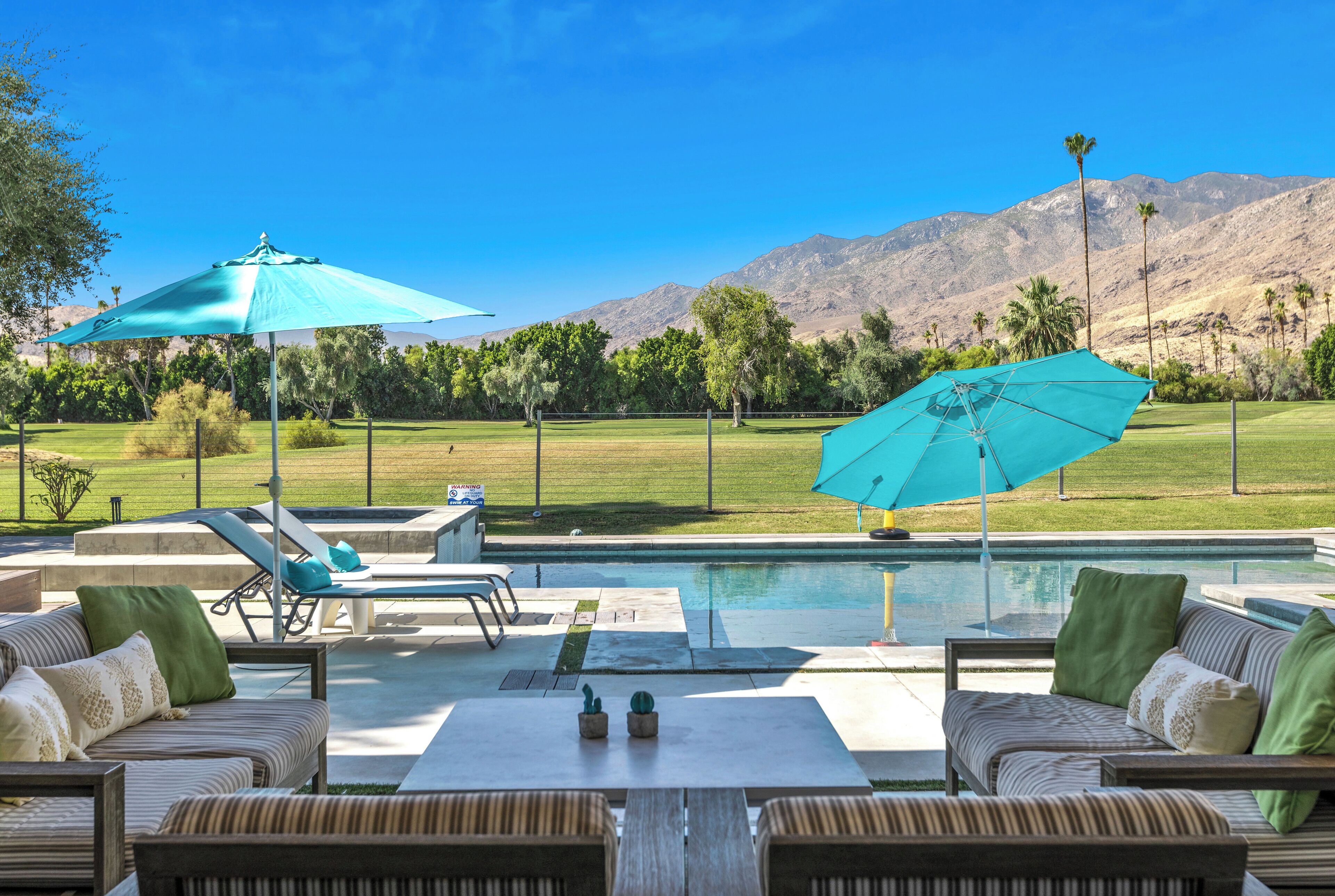 An outdoor patio with a pool, lounge chairs, and umbrellas.