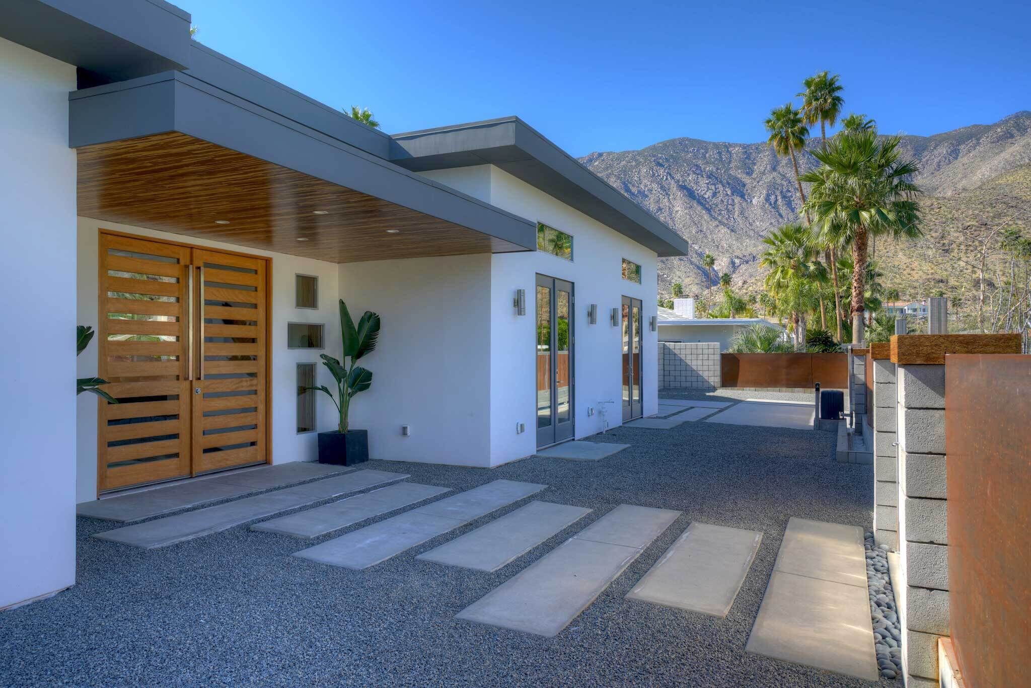 A modern house with a covered patio, a gravel driveway, and a mountain backdrop.