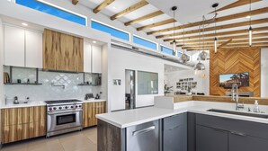 Una cucina moderna con un'isola grande, elettrodomestici in acciaio inossidabile, mobili in legno e una parete di fondo con decorazione a spina di pesce.