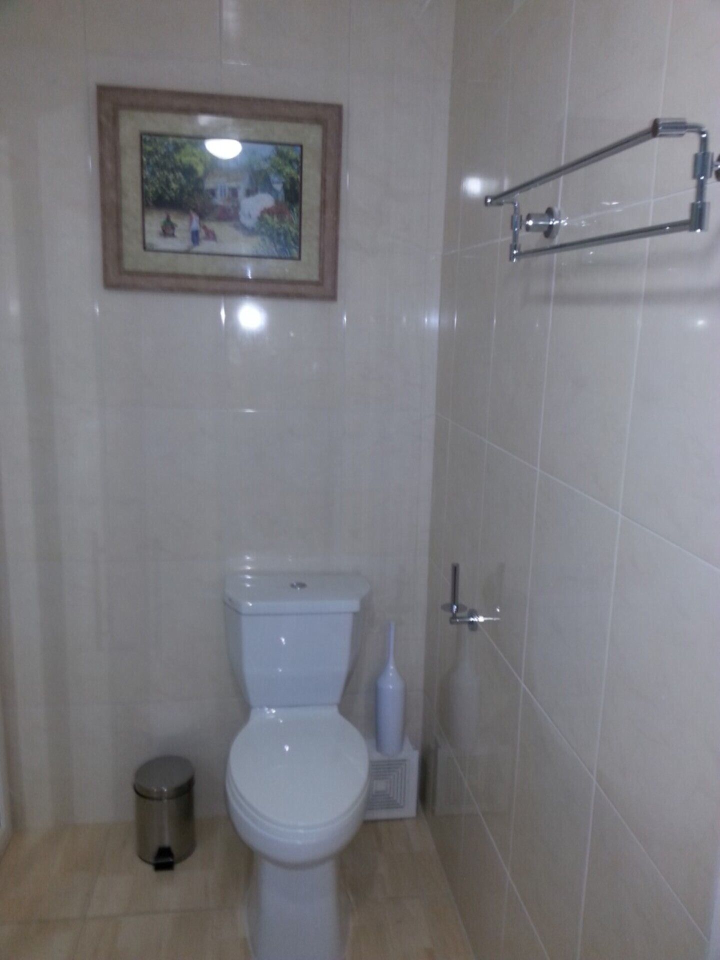 A bathroom with a toilet, a trash can, and a framed picture on the wall.