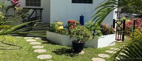 Een wit huis met een tuin, een stenen pad, potplanten en een fontein.