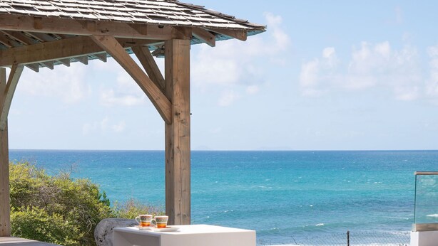 A wooden deck with a pool, a glass enclosure, and a view of the ocean. - Exceptional villa with sea view, infinity pool -Sainte Anne-12 people (Sainte Anne)