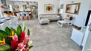 A spacious living area with a dining table, sofa, and kitchen in the background. - Exceptional villa with sea view, infinity pool -Sainte Anne-12 people (Sainte Anne)