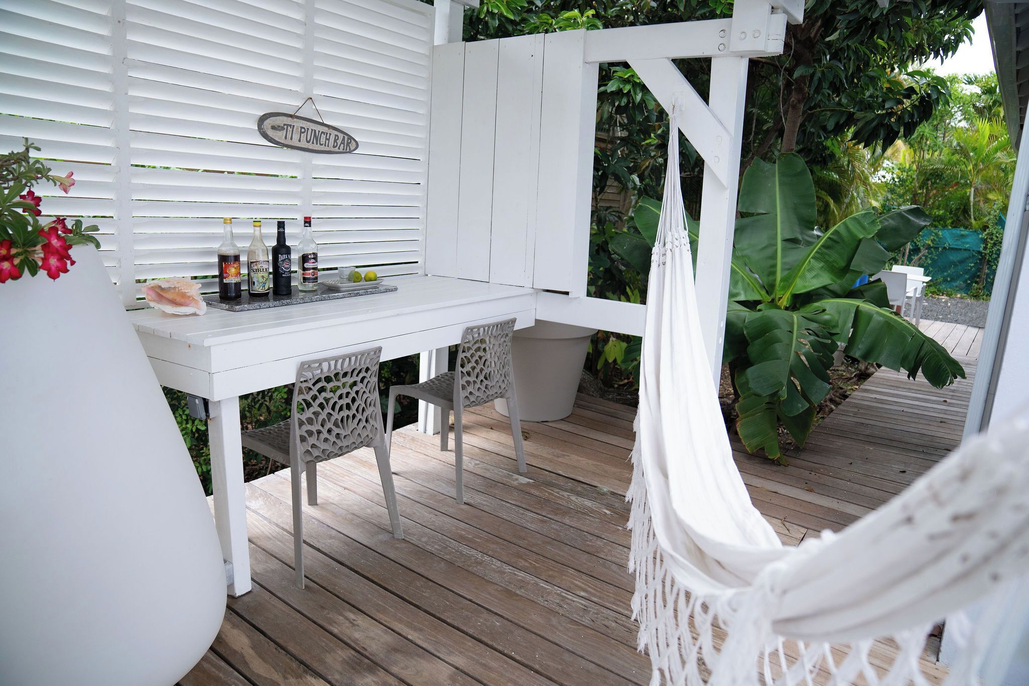 Uma área de estar ao ar livre com cadeiras e mesa, uma rede e um letreiro que diz 'TI PUNCH BAR'.