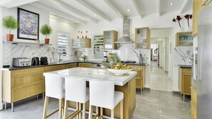 A modern kitchen with a marble countertop, wooden cabinets, and a central island with bar stools. - Exceptional villa with sea view, infinity pool -Sainte Anne-12 people (Sainte Anne)