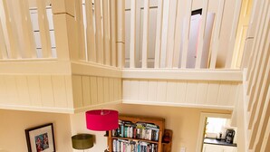 Un interior con varios niveles, una escalera, estanterías de madera, una lámpara roja y un cuadro en la pared.