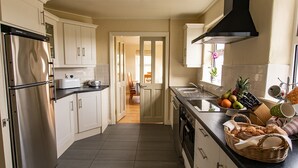 Cocina moderna con electrodomésticos de acero inoxidable, armarios blancos y una isla central con frutas y utensilios.