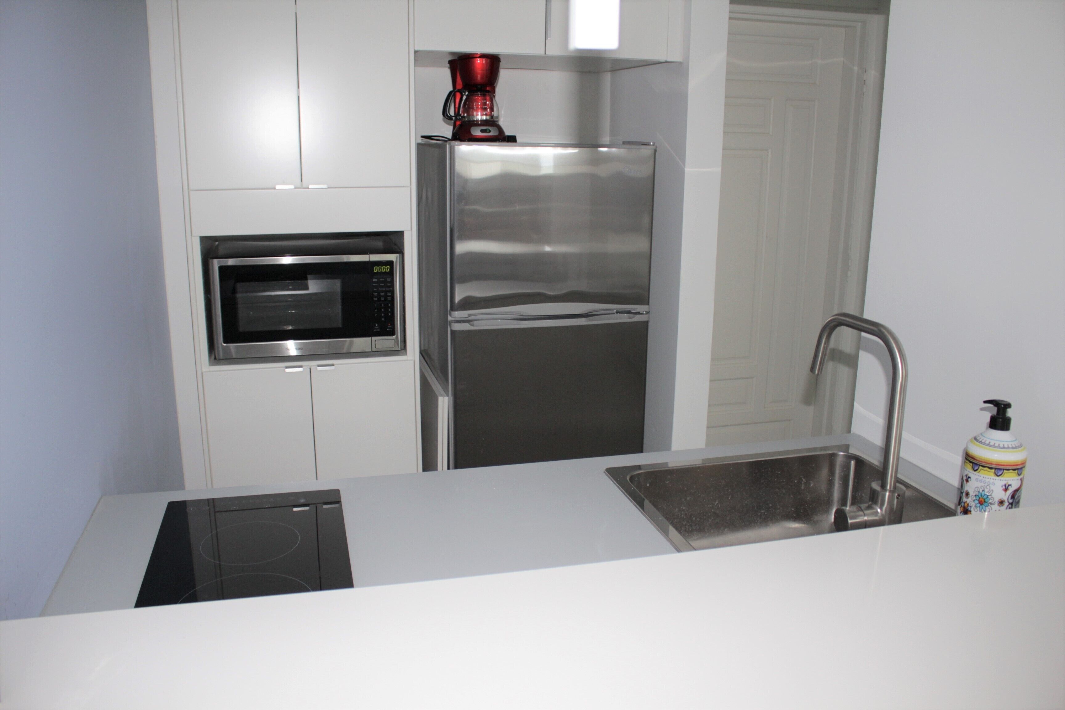 A compact kitchen with a microwave, stainless steel refrigerator, and a sink.