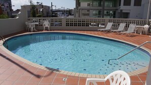 Ein Pool auf dem Dach mit weißen Stühlen und einem Tisch, umgeben von einem weißen Zaun.