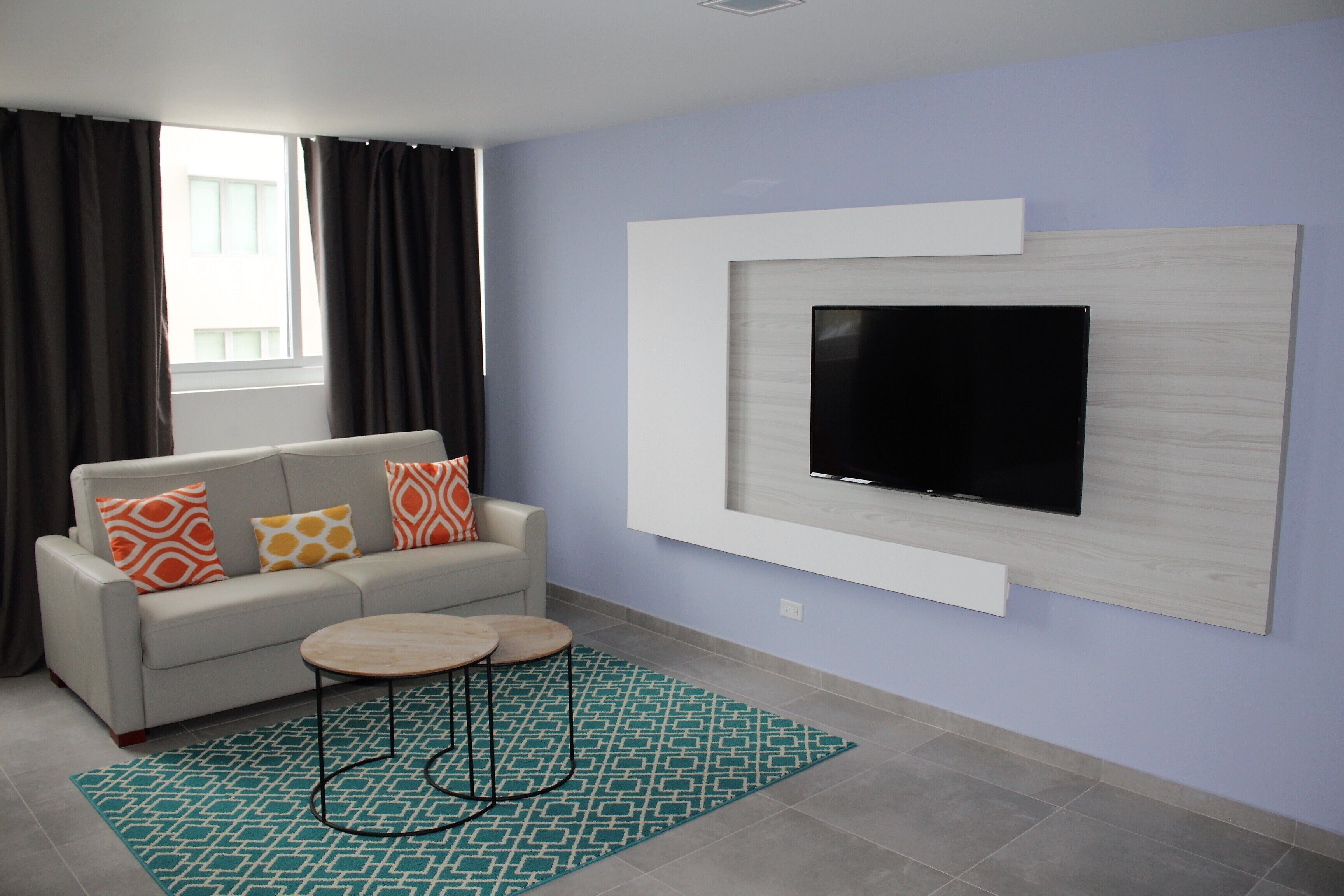A modern living room with a sofa, a coffee table, a TV mounted on the wall, and a patterned rug.