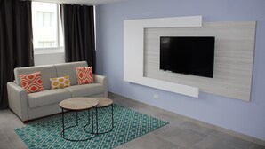 Ein modernes Wohnzimmer mit einer Couch, einem Couchtisch, einem an der Wand befestigten Fernseher und einem gemusterten Teppich.