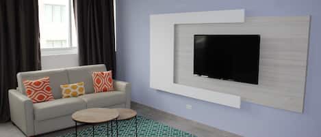 A modern living room with a sofa, a coffee table, a TV mounted on the wall, and a patterned rug.
