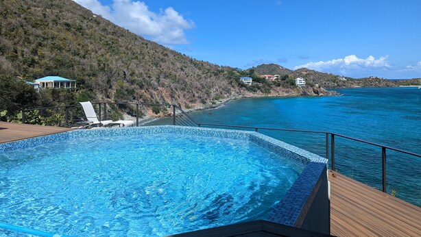 Una piscina con cubierta de madera, con vistas a una zona costera con casas y colinas.