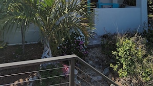 Una casa de dos pisos con un balcón, rodeada de vegetación y un cielo despejado.