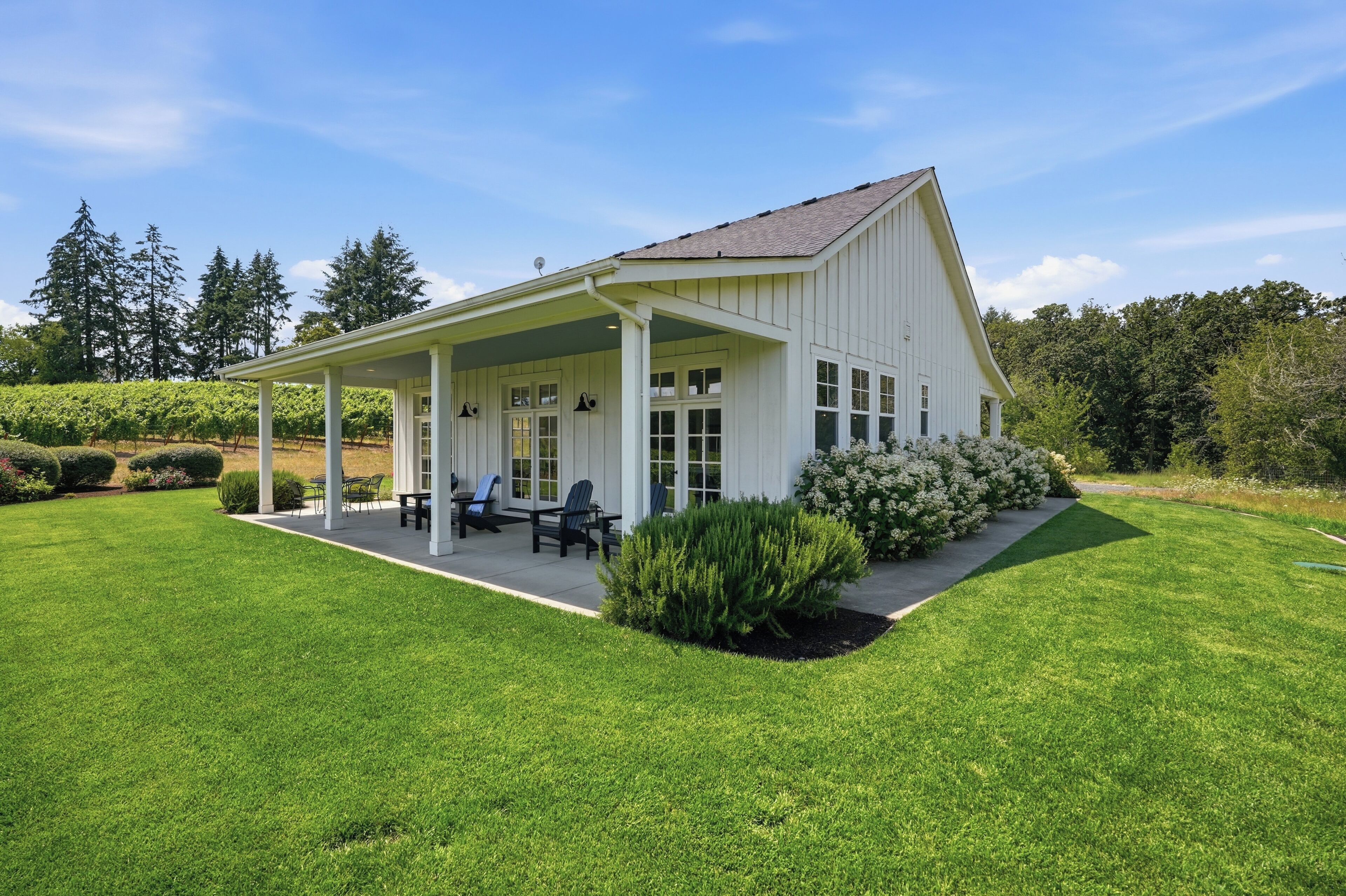 Een wit gebouw met een overdekte patio, zitplaatsen buiten en een verzorgd gazon.