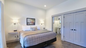 Une chambre à coucher avec un lit, des lampes de chevet, un tableau, une armoire et une salle de bain visible à travers une porte ouverte.