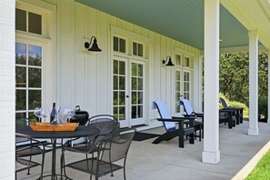 Ein überdachter Patio-Bereich mit Gartenmöbeln, darunter Stühle, Tische und ein Grill.