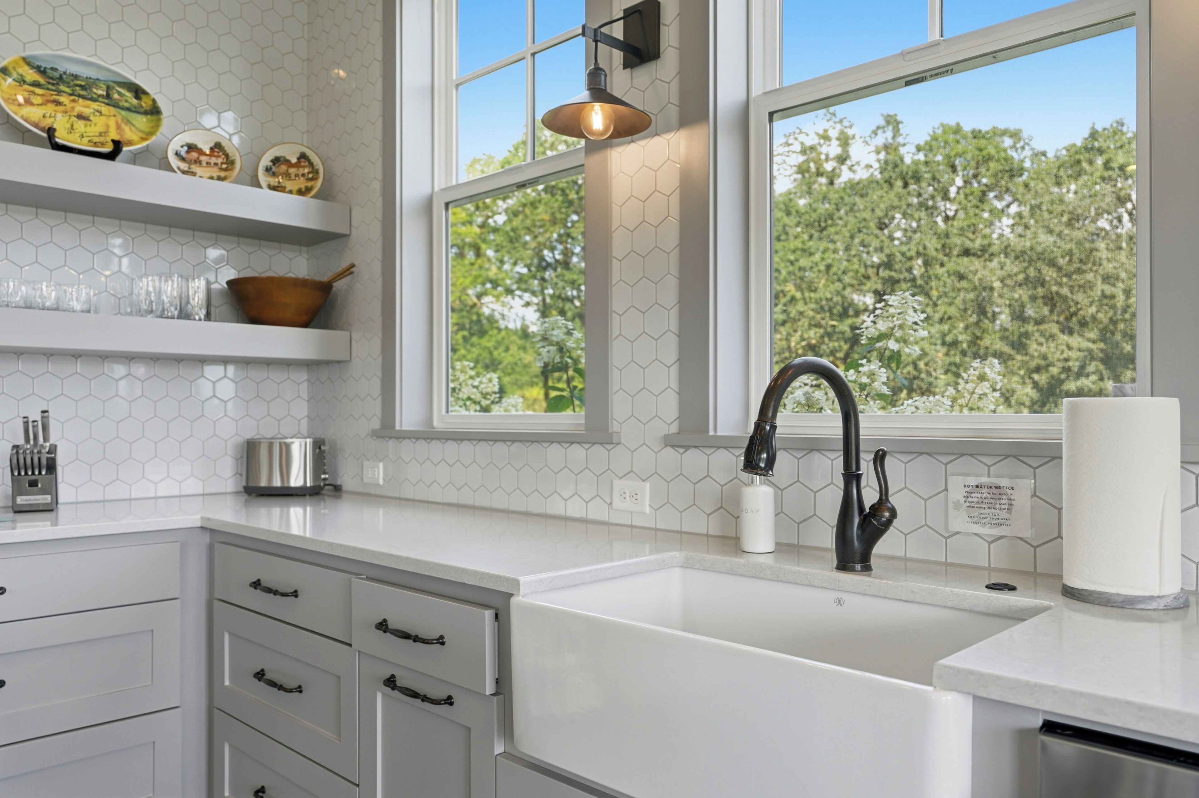 A kitchen with a white countertop, a black faucet, and a window with a view of trees.