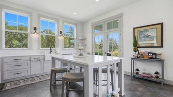 A modern kitchen with white cabinetry, a central island, and large windows offering views of greenery.