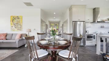 A modern kitchen with stainless steel appliances, a dining area with a round table and chairs, and a living room with a sofa and a decorative wall piece.