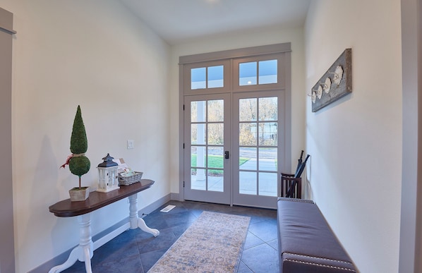 A hallway with a bench, a small table with decorative items, and a door with glass panels.