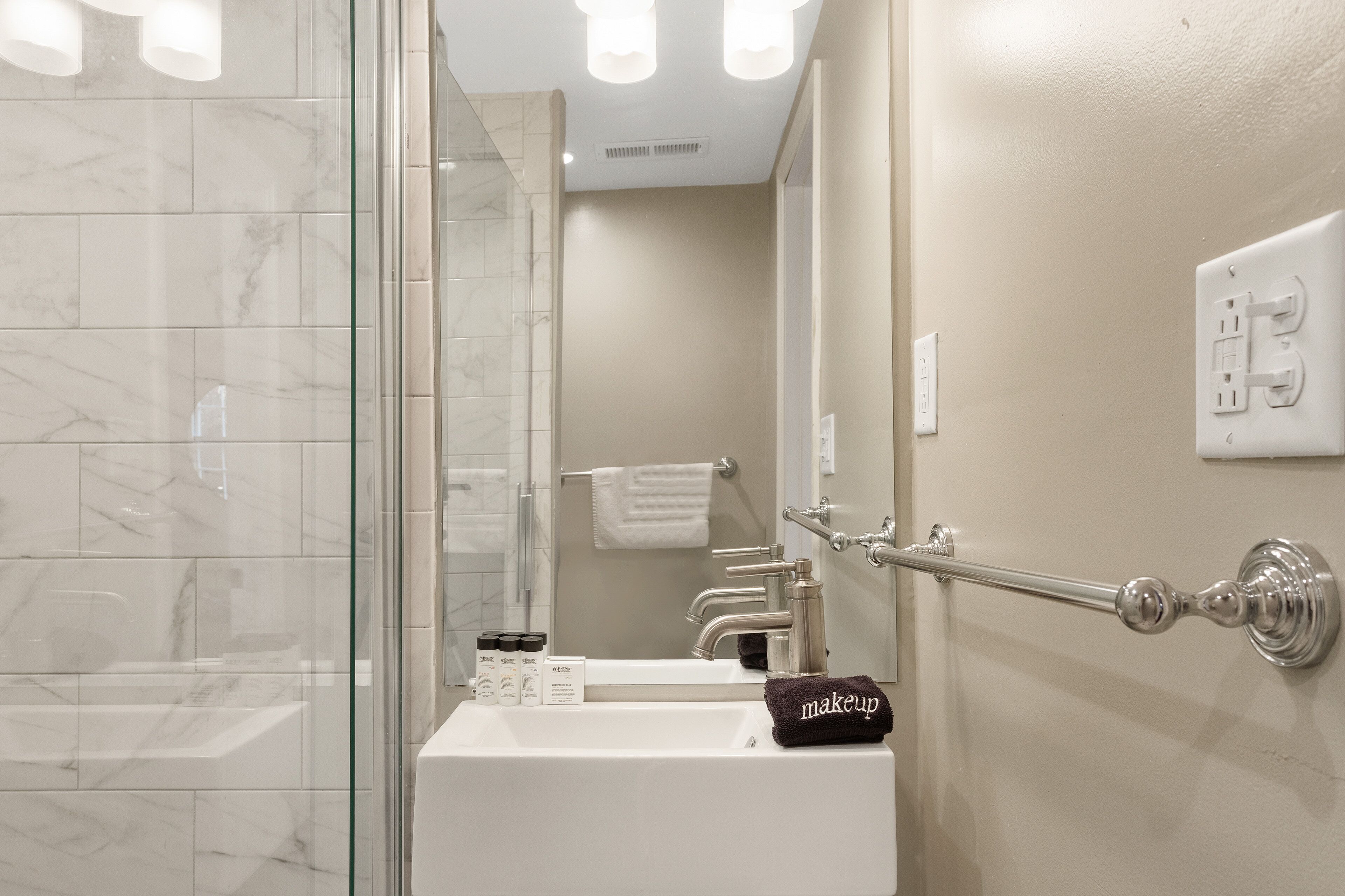 A bathroom with a glass shower enclosure, a white sink, and a towel rack with a makeup bag.