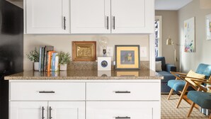 A kitchen with white cabinets, a countertop with books and a light bulb, and a blue chair in the background.