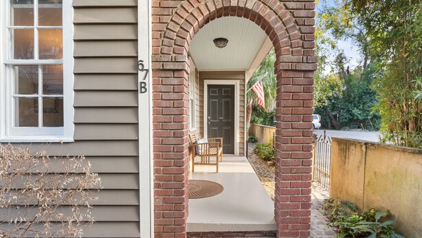 A brick archway leading to a front door with a bench and American flag outside.