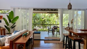 Un amplio salón con balcón, muebles de madera y una planta grande.