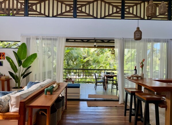 A spacious living area with a balcony, wooden furniture, and a large plant. - Beachside Designer Home with Pool (Puerto Viejo de Talamanca)