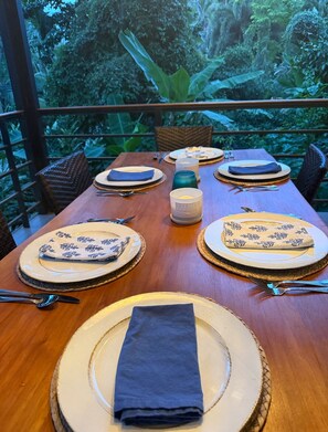 A dining table set for four with plates, cutlery, and napkins, overlooking a lush garden. - Beachside Designer Home with Pool Sleeps 8 (Puerto Viejo de Talamanca)