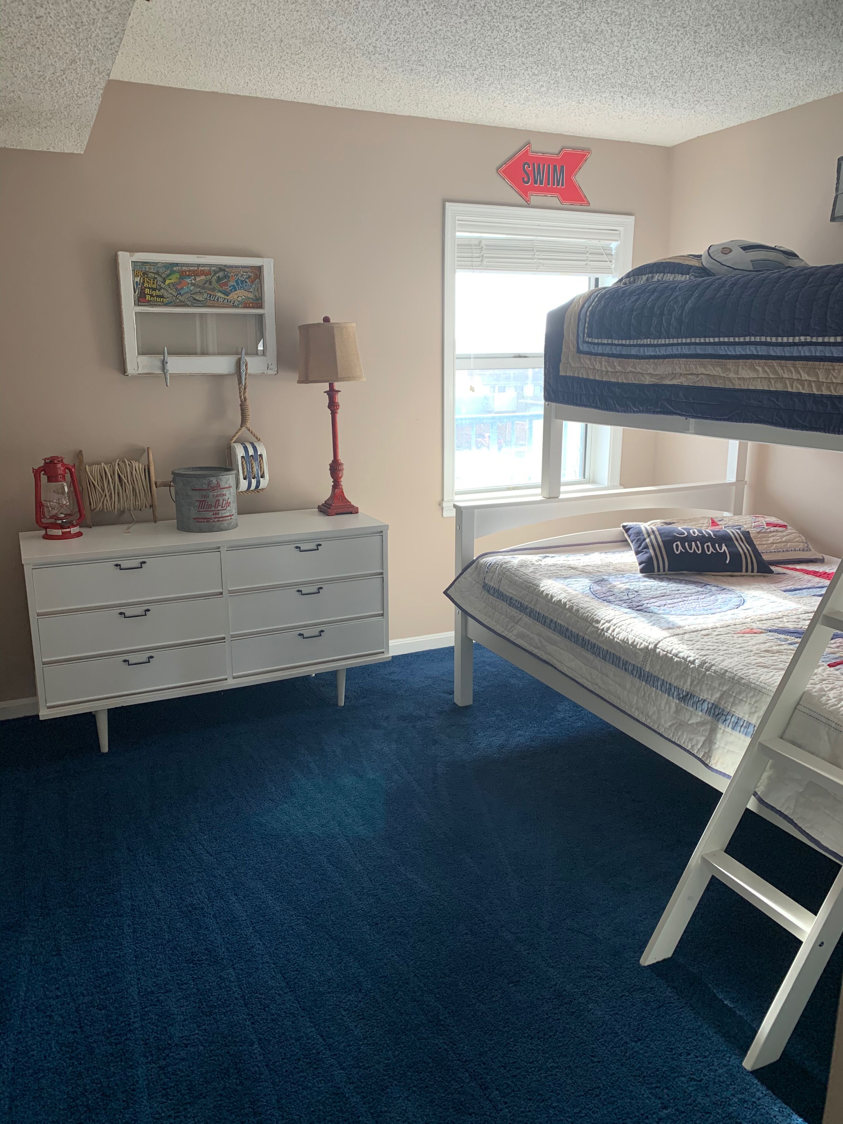 A bedroom with a bunk bed, a dresser, a map, a lamp, and a window.